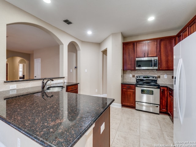 kitchen with decorative backsplash, appliances with stainless steel finishes, sink, dark stone countertops, and light tile patterned flooring