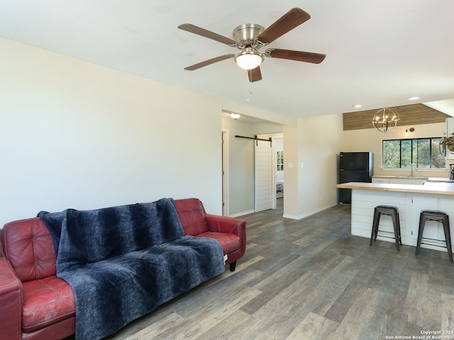 living room with ceiling fan with notable chandelier, a barn door, and dark hardwood / wood-style flooring