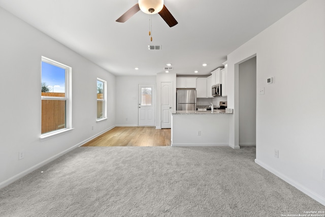 unfurnished living room featuring light carpet, sink, and ceiling fan