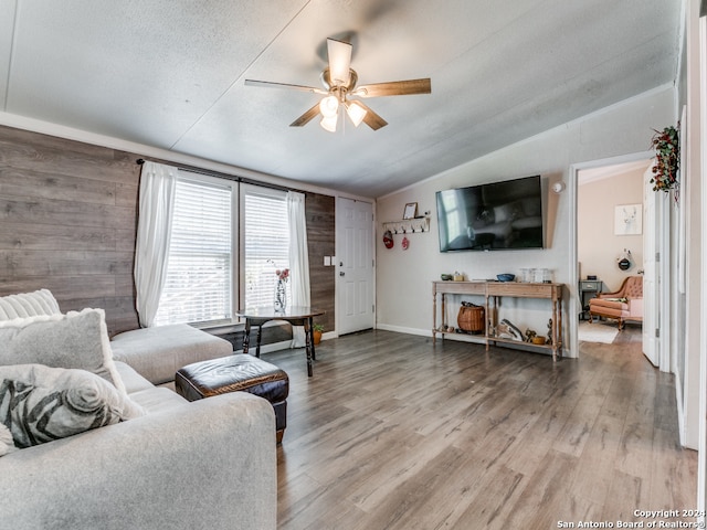 living room with a textured ceiling, ceiling fan, wooden walls, hardwood / wood-style flooring, and lofted ceiling