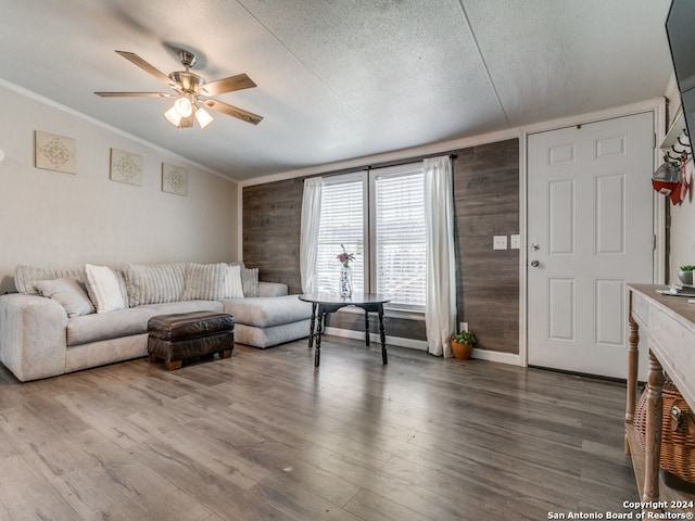 living room featuring ceiling fan, wood-type flooring, a textured ceiling, and wooden walls