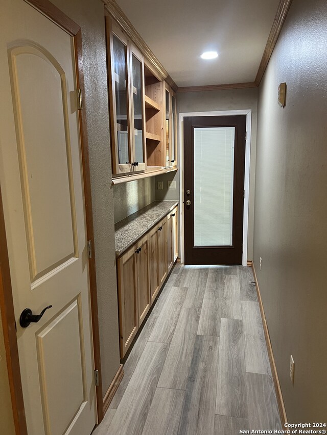 doorway to outside with baseboards, ornamental molding, and light wood-style floors