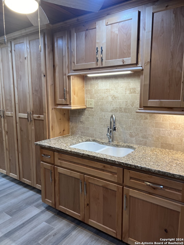 kitchen with light stone counters, light wood-type flooring, a sink, and tasteful backsplash