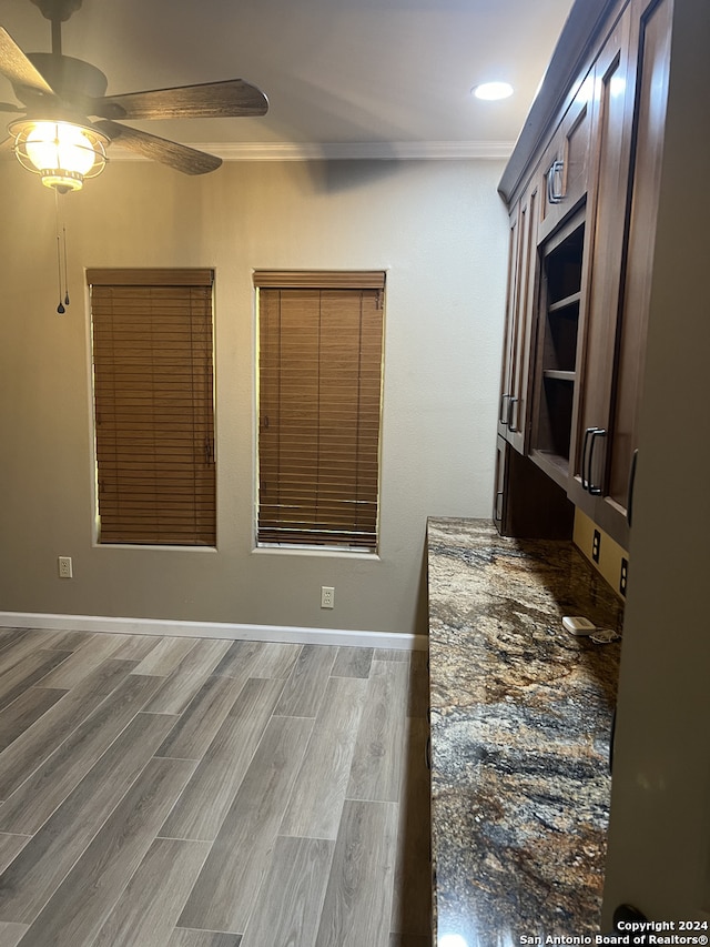 kitchen with ornamental molding, ceiling fan, dark stone countertops, wood finished floors, and baseboards