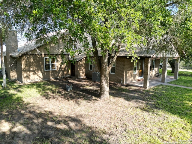 rear view of property with brick siding, a patio, a chimney, and a lawn