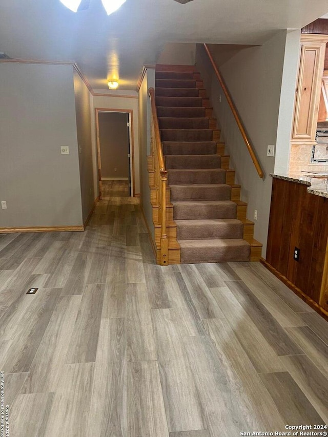 stairway with crown molding and wood finished floors