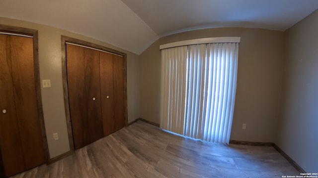 unfurnished bedroom featuring lofted ceiling, a closet, baseboards, and wood finished floors