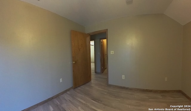 unfurnished room with vaulted ceiling, light wood-type flooring, and baseboards