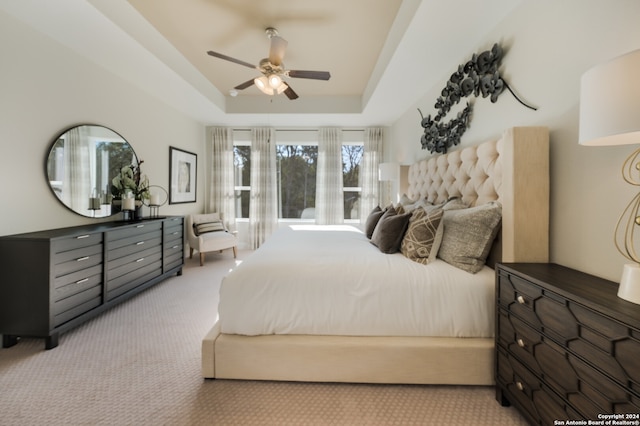 carpeted bedroom with ceiling fan and a raised ceiling