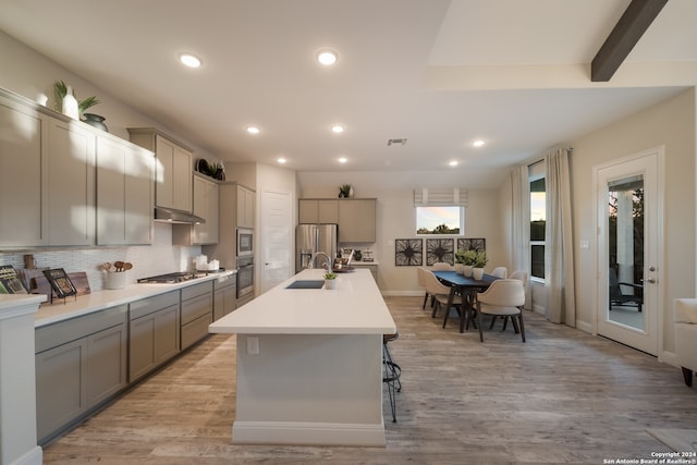 kitchen featuring backsplash, light wood-type flooring, gray cabinets, a center island with sink, and appliances with stainless steel finishes