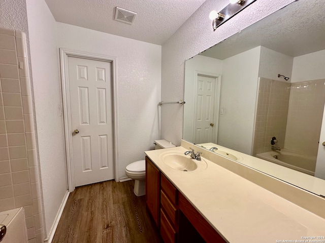 full bathroom featuring wood-type flooring, a textured ceiling, toilet, vanity, and tiled shower / bath