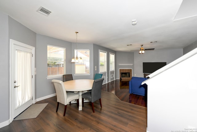 dining area with ceiling fan with notable chandelier, dark wood-type flooring, and a tiled fireplace