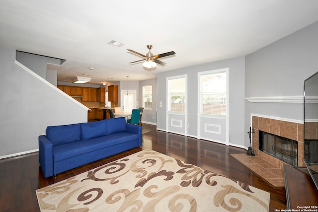 living room with ceiling fan, dark hardwood / wood-style flooring, and a tiled fireplace