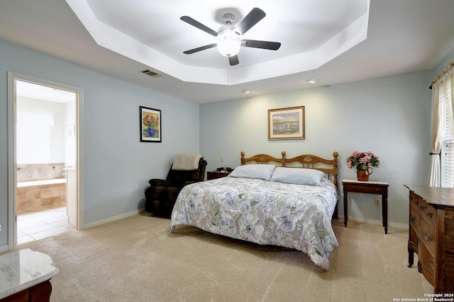 bedroom with light carpet, a raised ceiling, ensuite bath, and ceiling fan