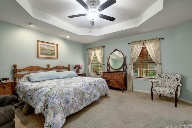 carpeted bedroom featuring a tray ceiling and ceiling fan