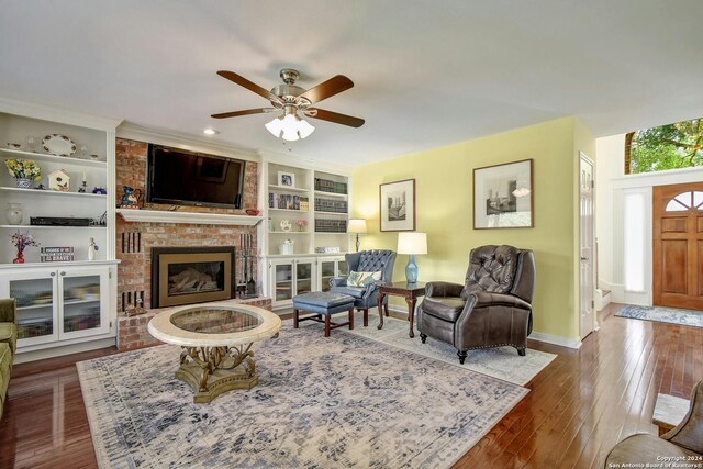 living room with ceiling fan, built in features, dark wood-type flooring, and a brick fireplace