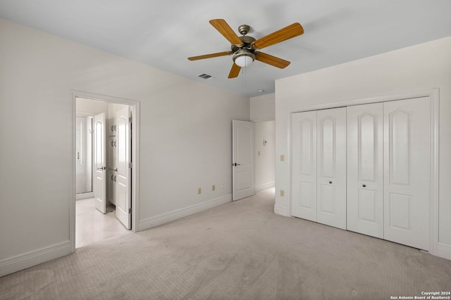 unfurnished bedroom featuring ceiling fan, light colored carpet, a closet, and ensuite bath