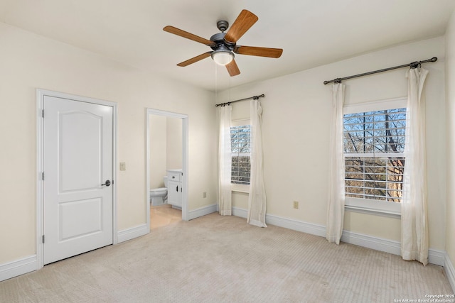 unfurnished bedroom featuring ceiling fan, light colored carpet, and ensuite bath