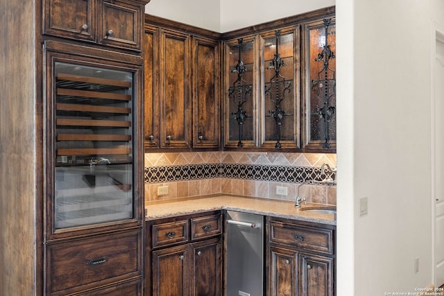 bar with wine cooler, sink, dark brown cabinets, and light stone countertops