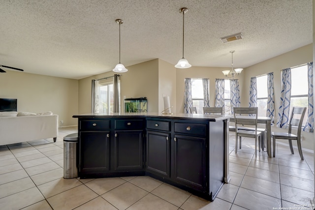 kitchen featuring pendant lighting, light tile patterned floors, an island with sink, and a textured ceiling