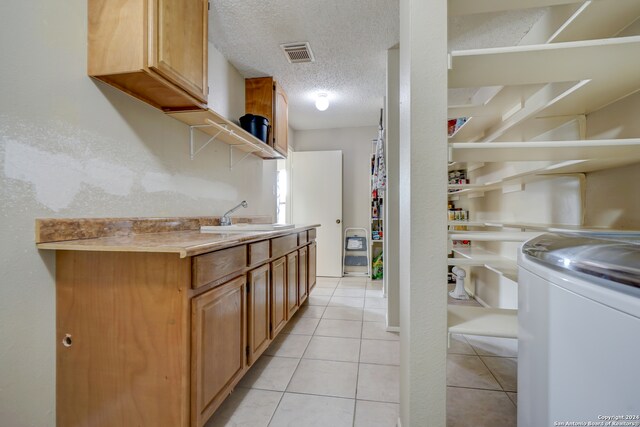 laundry room with cabinets, a textured ceiling, sink, washer / dryer, and light tile patterned flooring