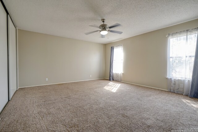 carpeted empty room featuring ceiling fan, plenty of natural light, and a textured ceiling