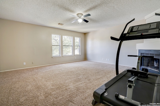 workout area with a fireplace, a textured ceiling, carpet floors, and ceiling fan