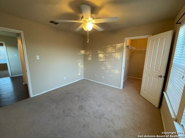 unfurnished bedroom featuring carpet flooring, a spacious closet, a closet, and ceiling fan