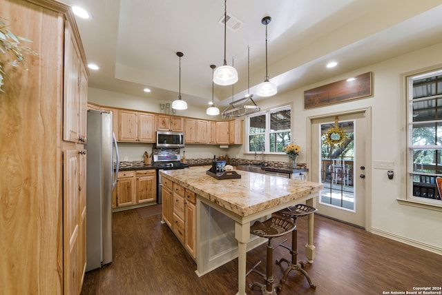 kitchen featuring pendant lighting, dark wood-type flooring, appliances with stainless steel finishes, a kitchen island, and a breakfast bar area