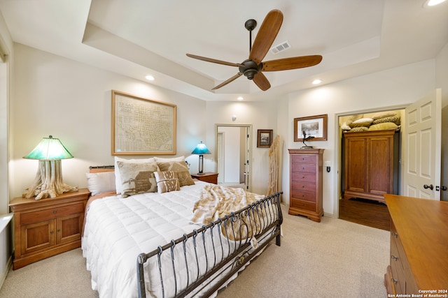 bedroom with light colored carpet, a raised ceiling, and ceiling fan