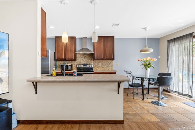 kitchen featuring decorative light fixtures, light wood-type flooring, wall chimney range hood, and appliances with stainless steel finishes