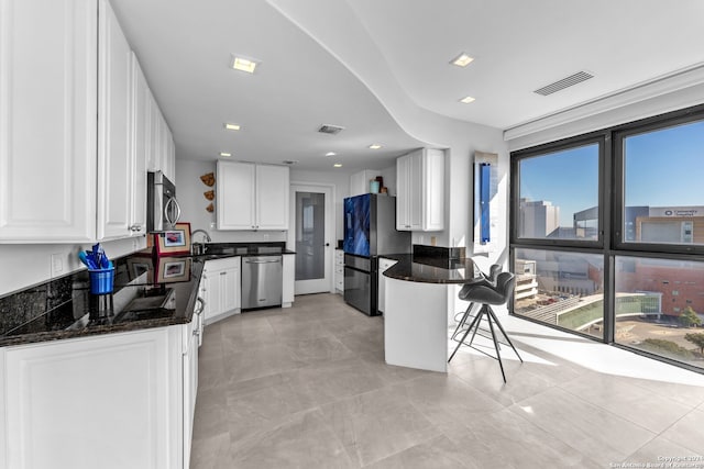 kitchen featuring appliances with stainless steel finishes, a breakfast bar, sink, dark stone countertops, and white cabinets