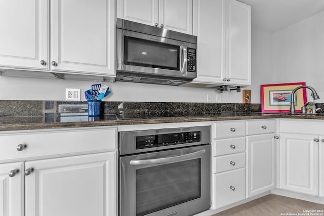 kitchen featuring white cabinets, stainless steel appliances, dark stone countertops, and sink