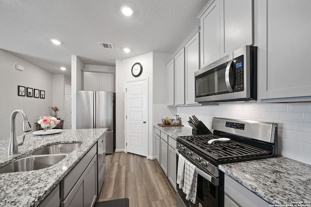 kitchen featuring dark wood-type flooring, sink, decorative backsplash, light stone counters, and stainless steel appliances