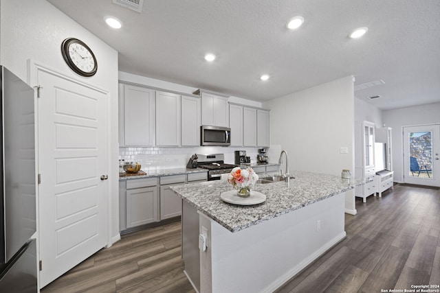 kitchen featuring light stone countertops, stainless steel appliances, an island with sink, and dark wood-type flooring