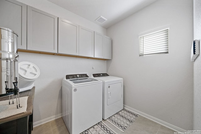 clothes washing area with washing machine and dryer, light tile patterned floors, and cabinets