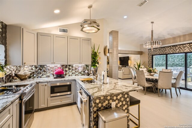 kitchen with pendant lighting, stainless steel appliances, vaulted ceiling, and light stone counters