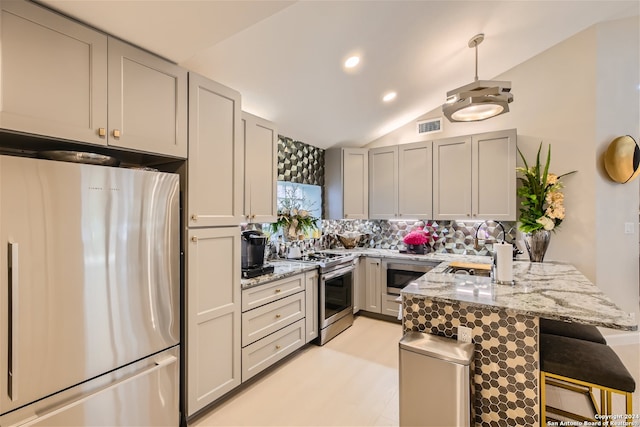 kitchen with light stone countertops, stainless steel appliances, vaulted ceiling, decorative light fixtures, and decorative backsplash