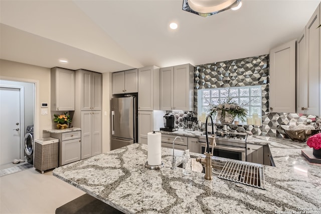 kitchen with appliances with stainless steel finishes, gray cabinets, vaulted ceiling, and light stone counters