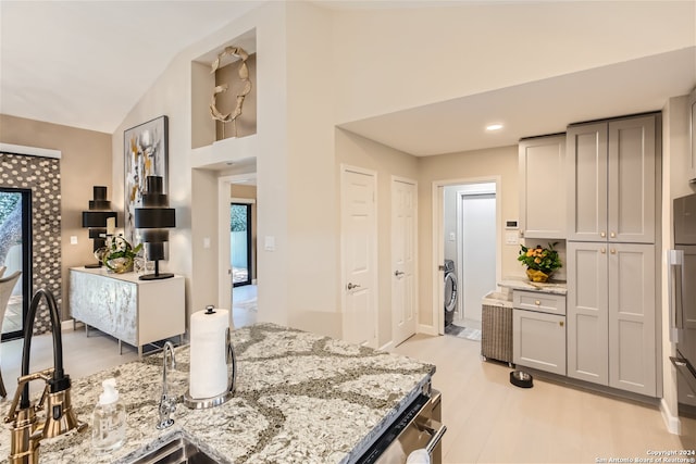 kitchen featuring gray cabinetry, light stone countertops, light hardwood / wood-style flooring, and vaulted ceiling