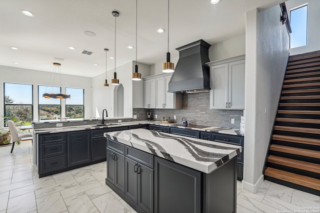 kitchen featuring tasteful backsplash, custom range hood, sink, decorative light fixtures, and a center island