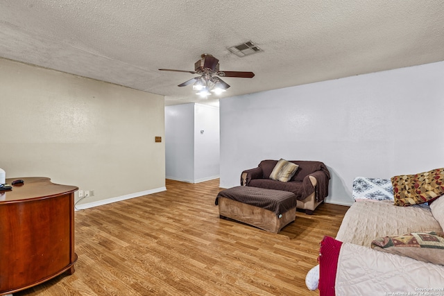 living room with ceiling fan, a textured ceiling, and light wood-type flooring