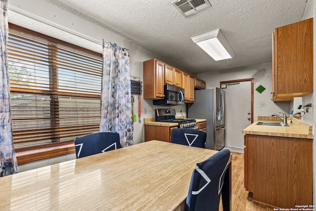 kitchen with appliances with stainless steel finishes, a textured ceiling, light hardwood / wood-style flooring, and sink