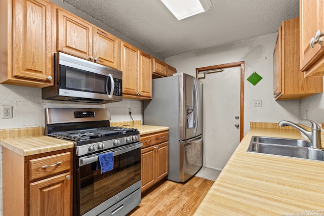 kitchen featuring appliances with stainless steel finishes, light wood-type flooring, a textured ceiling, and sink