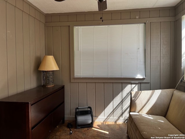 living area featuring ceiling fan and wood walls