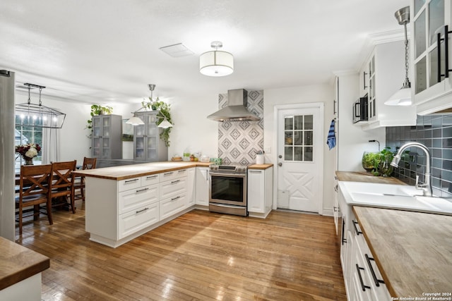 kitchen with stainless steel range with electric stovetop, light wood-style flooring, butcher block counters, wall chimney range hood, and glass insert cabinets