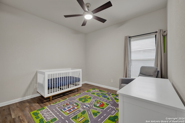 bedroom with a nursery area, dark wood-type flooring, and ceiling fan