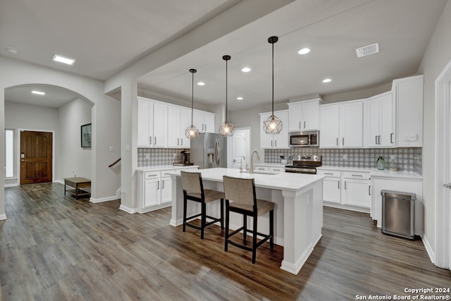 kitchen featuring pendant lighting, hardwood / wood-style floors, white cabinets, tasteful backsplash, and stainless steel appliances