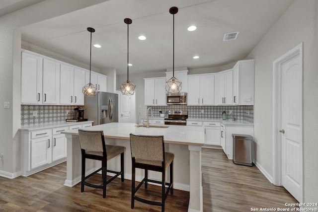 kitchen featuring stainless steel appliances, pendant lighting, a kitchen island with sink, white cabinets, and light wood-type flooring