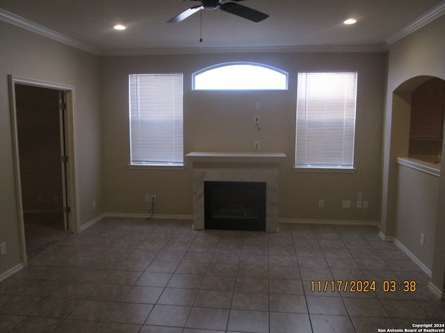 unfurnished living room with tile patterned flooring, ceiling fan, ornamental molding, and a high end fireplace